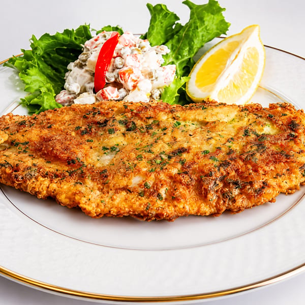 Golden-brown fried fish fillet with a side of potato salad, lettuce, and a lemon wedge.