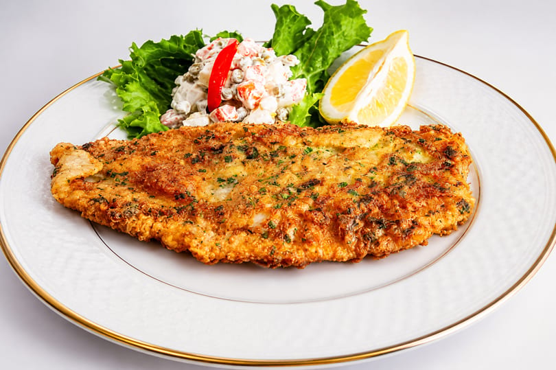 Golden-brown fried fish fillet with a side of potato salad, lettuce, and a lemon wedge.