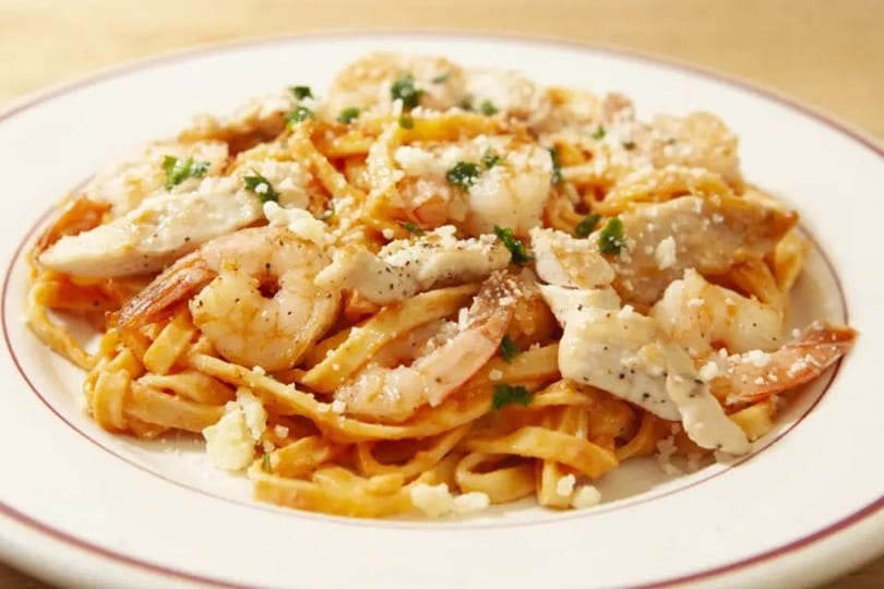 Fettuccine pasta with shrimp, chicken, and parmesan cheese on a white plate.