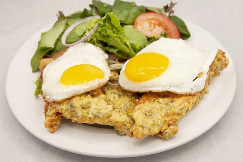 Two fried eggs on breaded cutlets with a side salad of greens, tomato, and red onion.