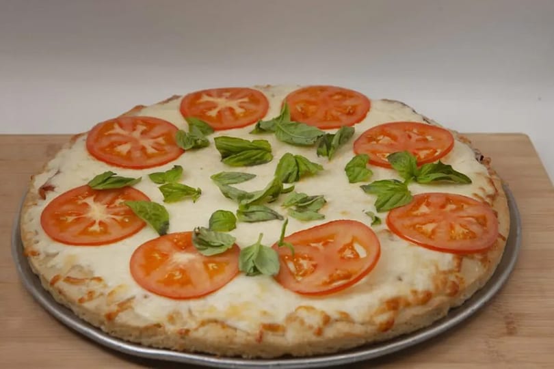 Round pizza with melted cheese, sliced tomatoes, and fresh basil leaves on a wooden board.