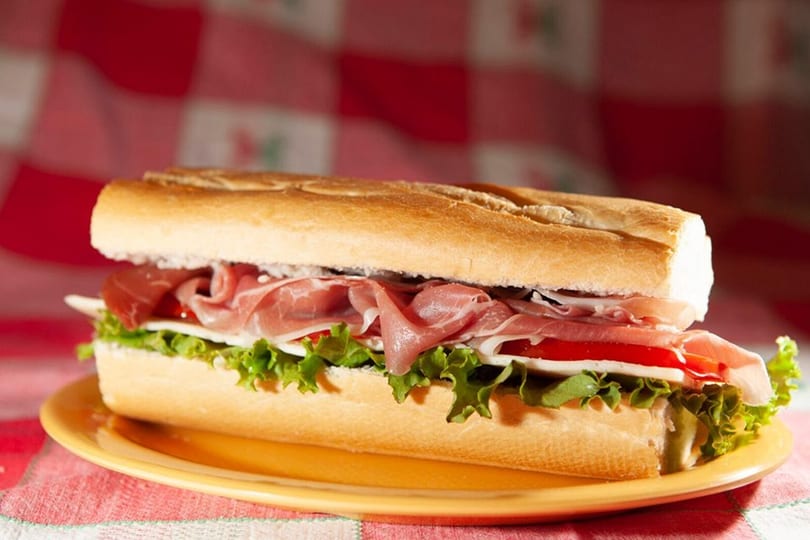 A large submarine sandwich with prosciutto, lettuce, tomatoes, and cheese on a yellow plate.