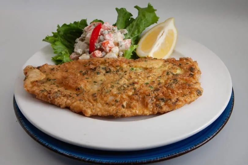 Crispy fried fish with a side of creamy salad and a fresh lemon slice.